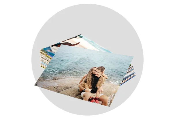 Stack of photo prints with a picture of a couple cuddling by the ocean on top. Get your best pics printed on high-quality photo paper!