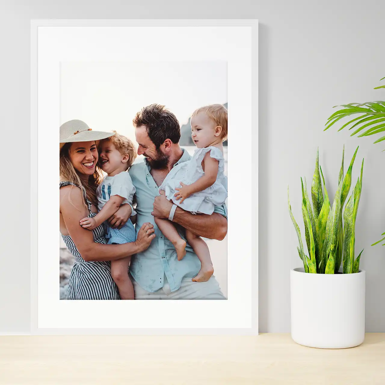 Order poster prints and add more personality to your home. A framed poster print showing a young family is standing on a sideboad with a plant next to it. Order your poster and add a frame to it.